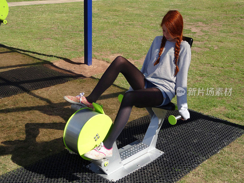 女孩在健身馆-公园里骑着健身车/自行车锻炼的画面